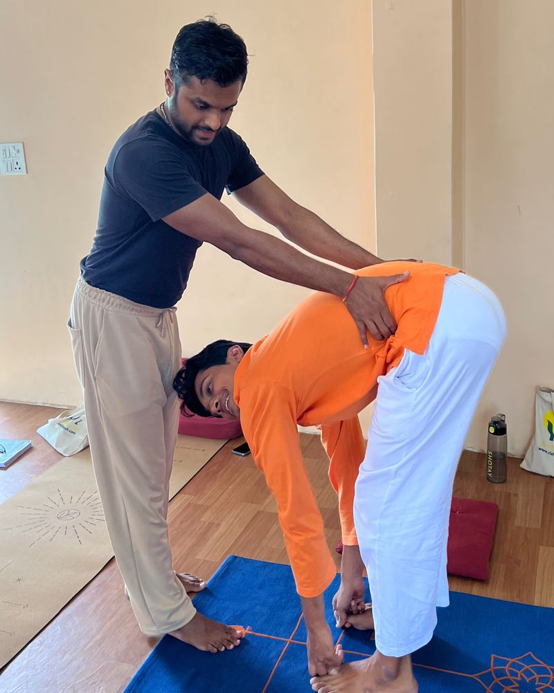 Prathamesh Chavan guiding a student through a standing forward fold